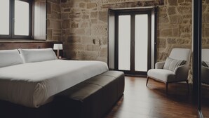 Un dormitorio con una cama grande, una silla, una mesita de noche y una pared de piedra.