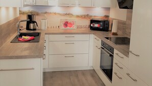 A modern kitchen with white cabinets, a wooden countertop, a coffee maker, a microwave, and a built-in oven.
