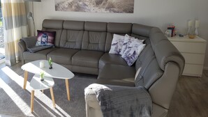 A modern living room with a grey leather sofa, a white coffee table, and a painting of a beach scene.