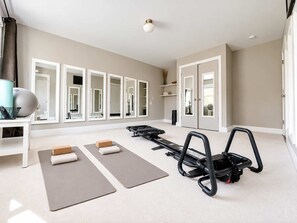 Een ruime kamer met trainingsapparatuur, waaronder een loopband en hometrainers, en een grote spiegelwand.