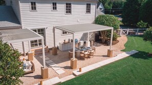 Een terras met een barbecue en eethoek, omgeven door een wit huis en een verzorgd gazon.