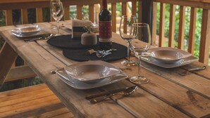 A wooden table set for dining with plates, glasses, and a bottle, surrounded by a wooden deck and a moss-covered tree. - Casa del Roble Avandaro (Valle de Bravo)