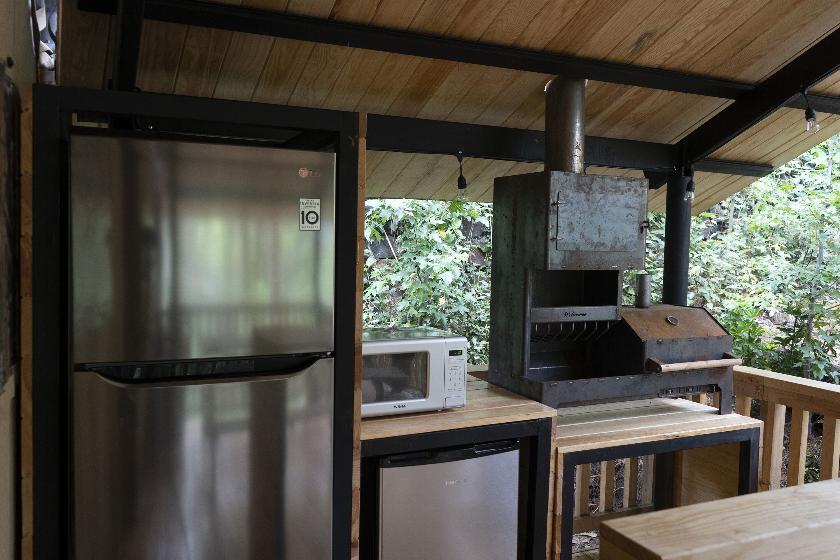 Una cocina compacta con refrigerador de acero inoxidable, microondas y parrilla integrada.