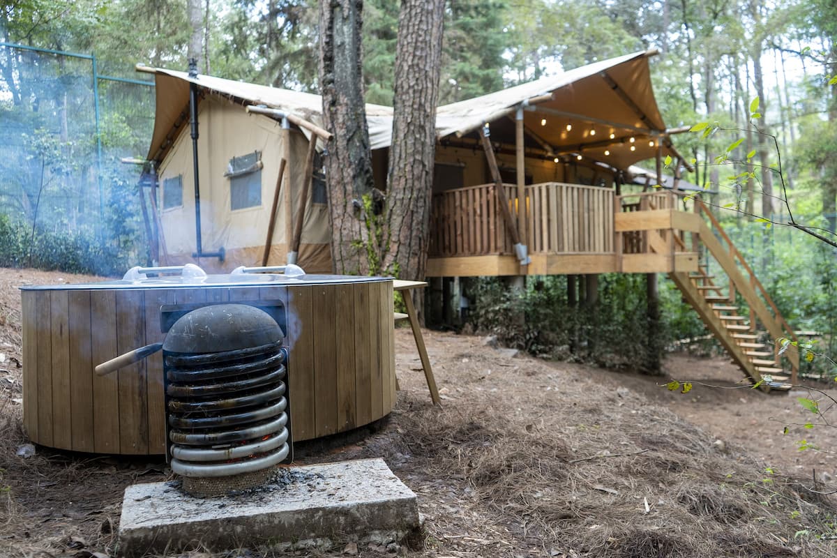 A rustic wooden cabin with a hot tub, surrounded by trees and a wooden deck.