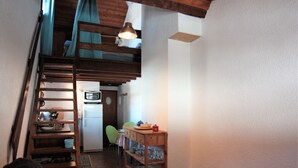 Une pièce compacte avec un escalier en bois, un coin cuisine, un espace repas avec une chaise et une petite table avec une lampe.