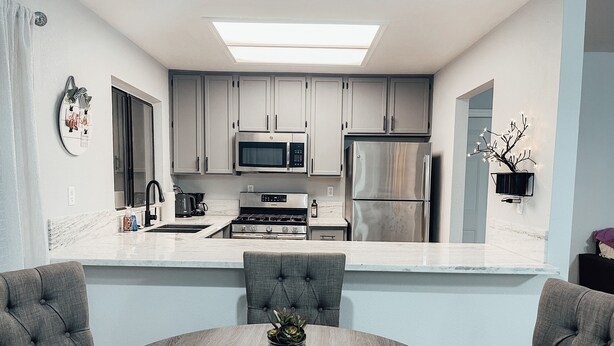 A modern kitchen with grey cabinets, a stainless steel refrigerator, a microwave, and a stove. There is a dining table with a vase of flowers and a decorative plate. - Entire beautiful 2 bedroom house (North Highlands)