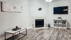A modern living room with a fireplace, a flat-screen TV, and a ceiling fan. - Entire beautiful 2 bedroom house (North Highlands)