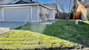 A residential house with a garage, a well-maintained lawn, and a wooden fence. - Entire beautiful 2 bedroom house (North Highlands)