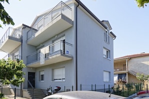 Un edificio residenziale a più piani con balconi, una scala e un'auto parcheggiata.