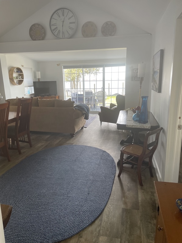A spacious living room with a large TV, a sofa, a dining area with chairs, and a view through glass doors to an outdoor patio.