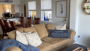 A cozy living room with a beige sofa, a coffee table, and a dining area in the background.