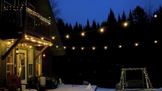Une terrasse enneigée, illuminée de guirlandes lumineuses, avec une balançoire en bois et un bonhomme de neige.