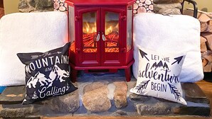Une cheminée en pierre avec un poêle à bois rouge, deux coussins décoratifs et une lanterne accrochée au mur.