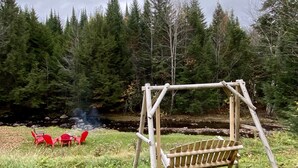 Un ensemble de balançoires en bois, installé dans un espace herbeux, avec des chaises rouges et un foyer au fond.