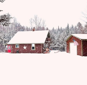 Une cabane en bois rouge, avec une porte blanche, un porche et un petit abri surmonté d’un drapeau américain.