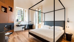 Una camera da letto con un letto a baldacchino, una scrivania con una sedia, una TV e una finestra vista alberi.