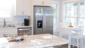 A modern kitchen with white cabinets, a stainless steel refrigerator, a coffee maker, and a breakfast bar. - V29 Family-friendly 3BR w/ Outdoor Kitchen + 2 Lounges, Limo Golf Cart (Myrtle Beach)