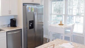 A kitchen with white cabinets, a stainless steel refrigerator, a coffee maker, and a dining area with a table and chairs. - V29 Family-friendly 3BR w/ Outdoor Kitchen + 2 Lounges, Limo Golf Cart (Myrtle Beach)