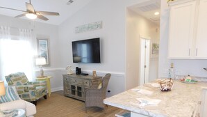 A living room with a television, a sofa, a chair, a small table, and a kitchen area with a counter and stools. - V29 Family-friendly 3BR w/ Outdoor Kitchen + 2 Lounges, Limo Golf Cart (Myrtle Beach)