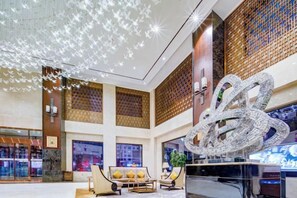 A spacious lobby with a large chandelier, seating area, and a decorative wall piece.