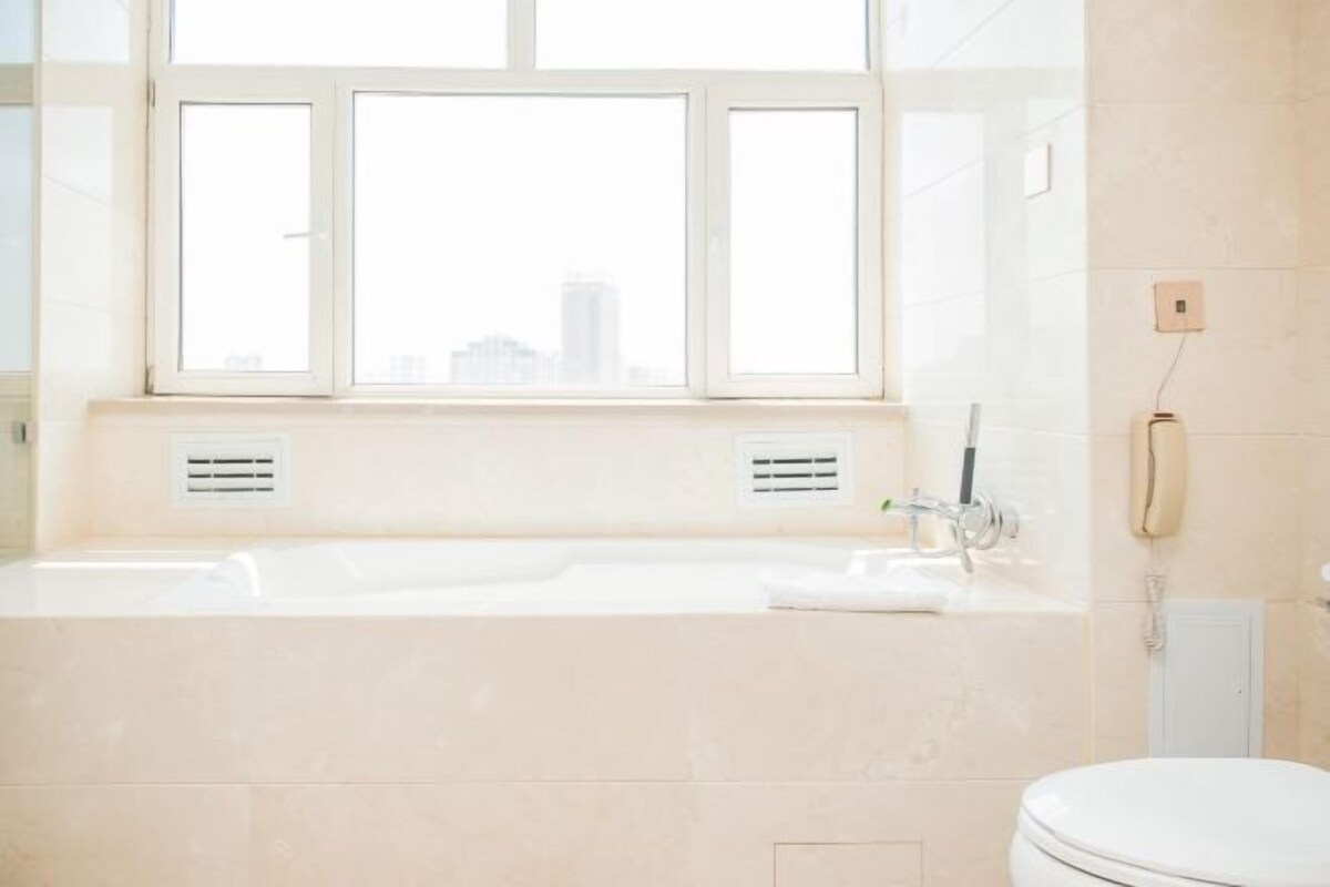 Un baño moderno con una bañera grande, un inodoro y un ventanal con vistas a la ciudad.