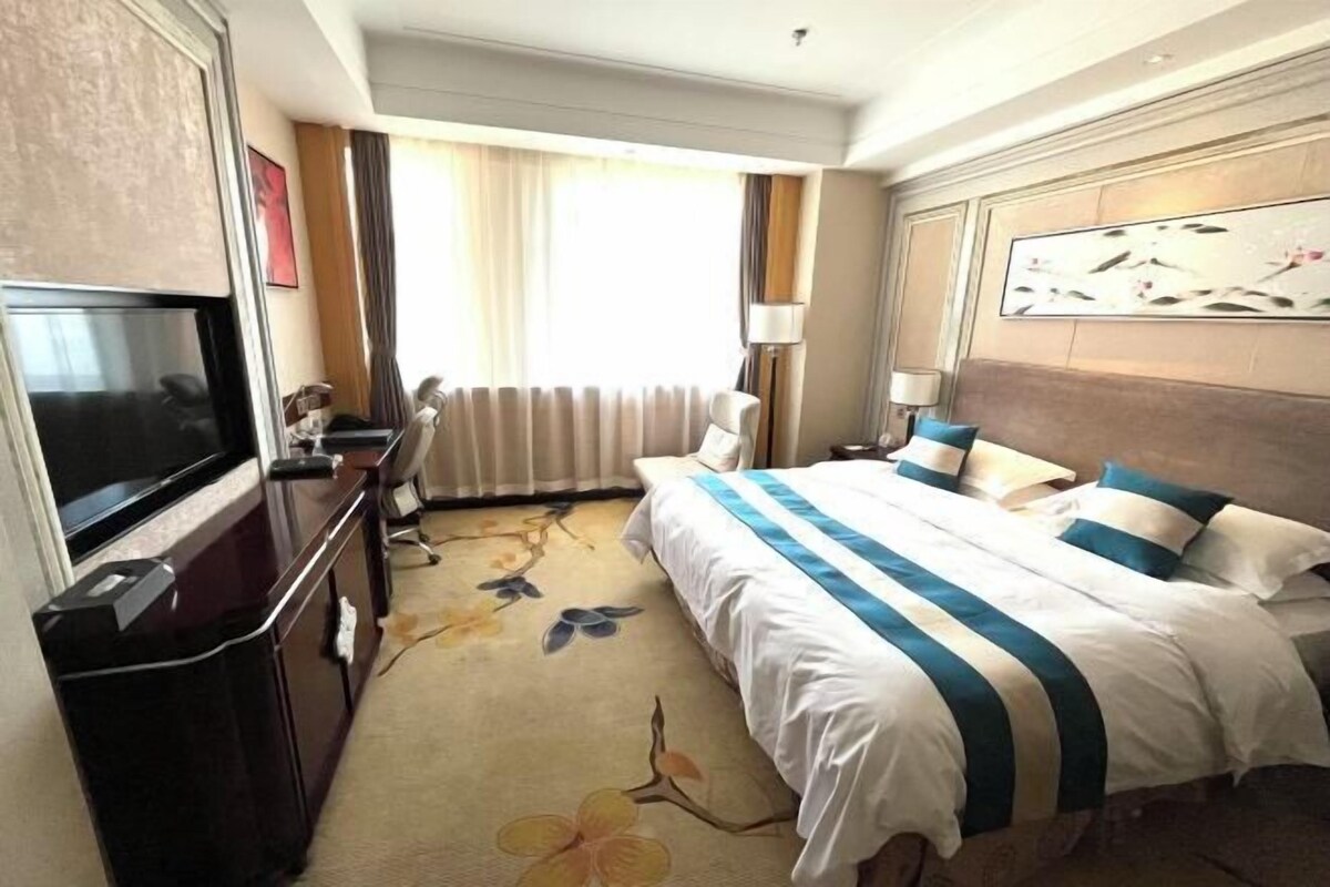 Habitación de hotel con una cama grande, televisión, escritorio y ventana con cortinas.