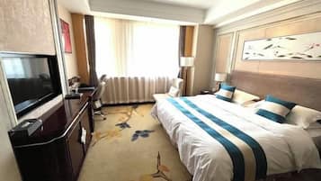 Habitación de hotel con una cama grande, televisión, escritorio y ventana con cortinas.
