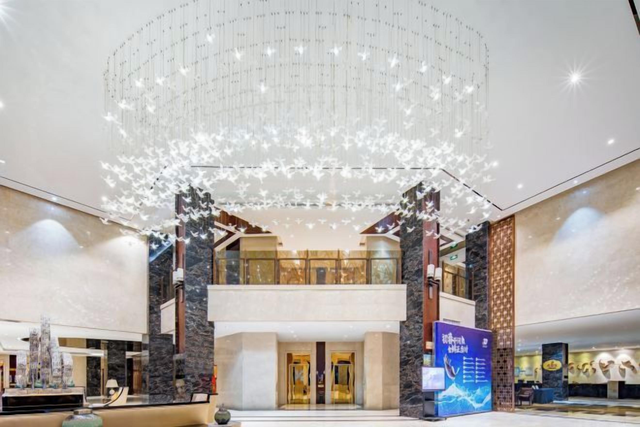 A spacious lobby with a high ceiling, a central chandelier, and a reception desk.