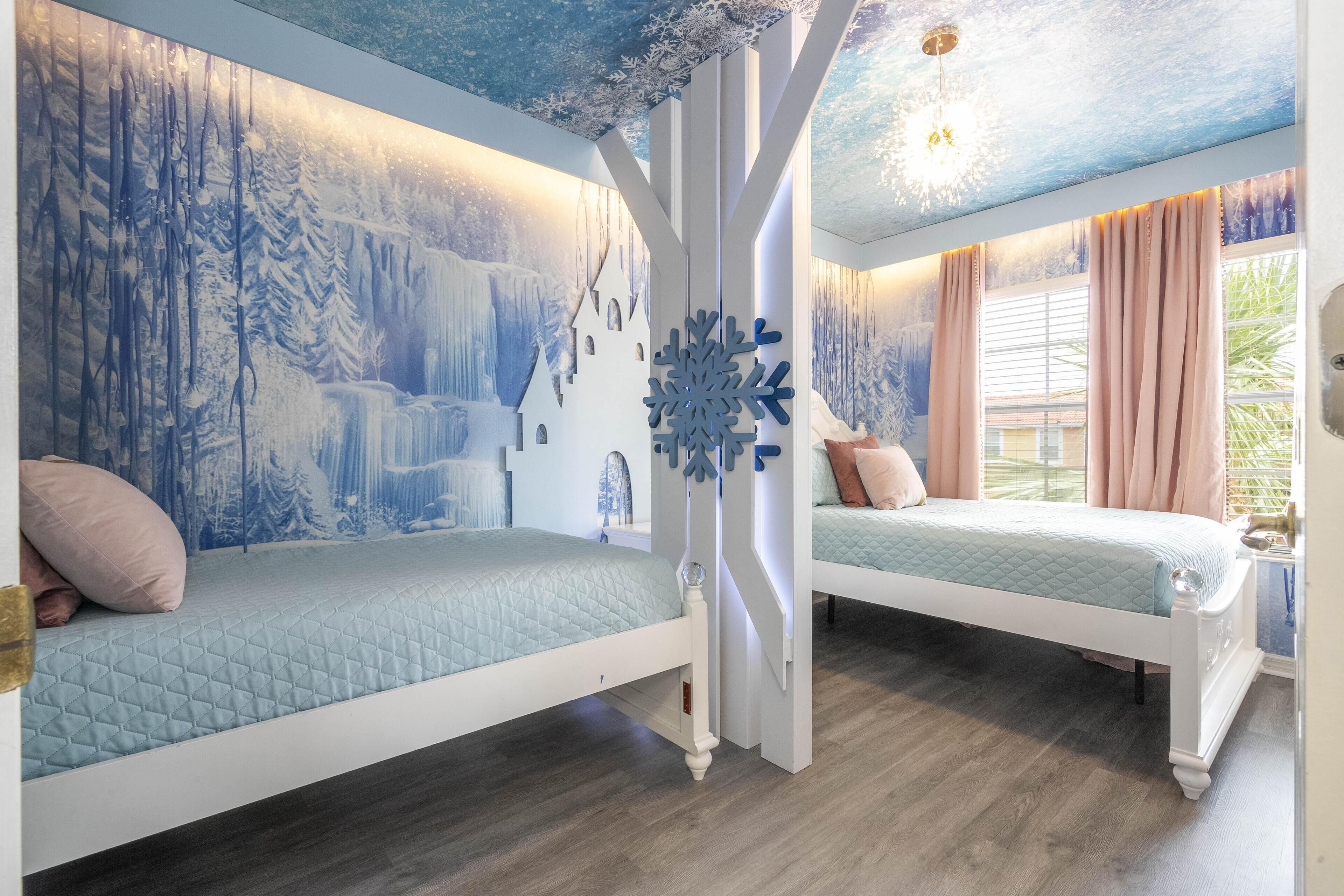 A bedroom with two beds, a large snowflake decoration, and a mural of a snowy landscape.