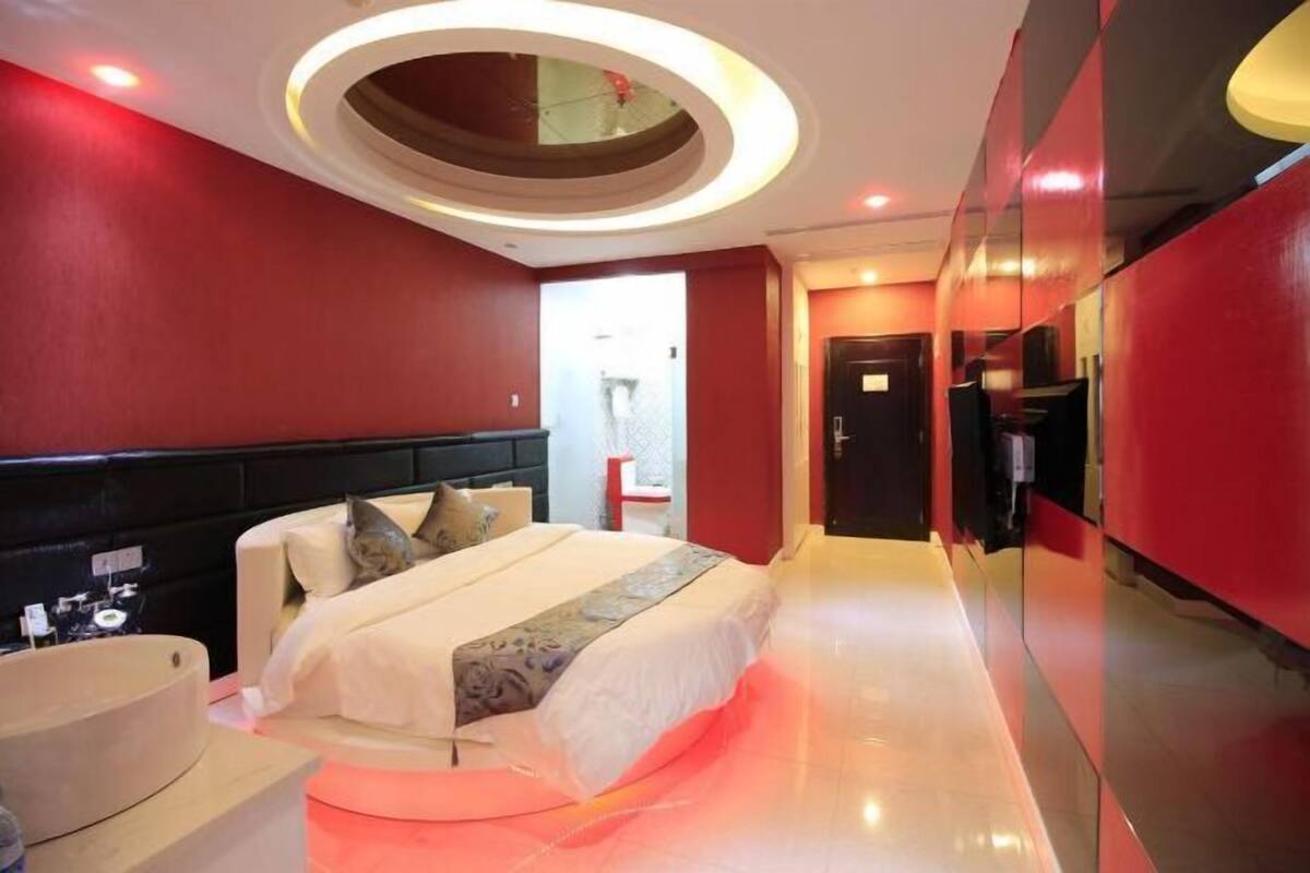 A modern hotel room with a large bed, a round mirror above the bed, and a red accent wall.