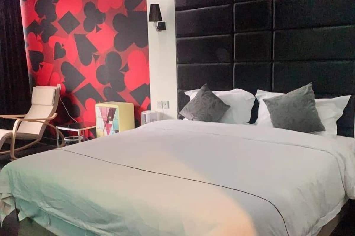 A hotel room with a large bed, a chair, a wall with a red and black pattern, and a black headboard.