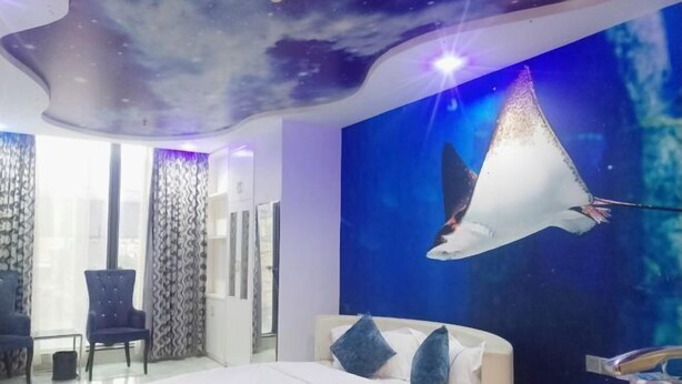 Un dormitorio con cama, mesita de noche, silla y un mural en la pared con un rayo mantarraya volando.