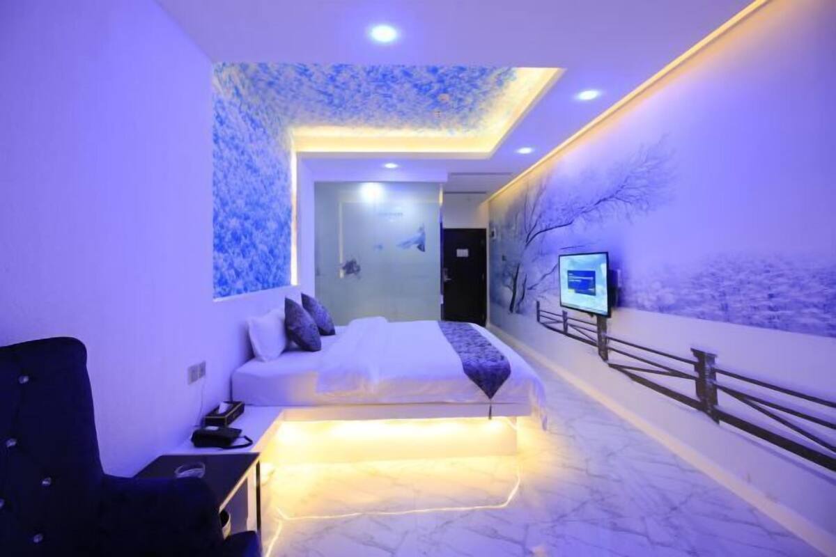 A modern hotel room with a bed, seating area, and a TV mounted on the wall.