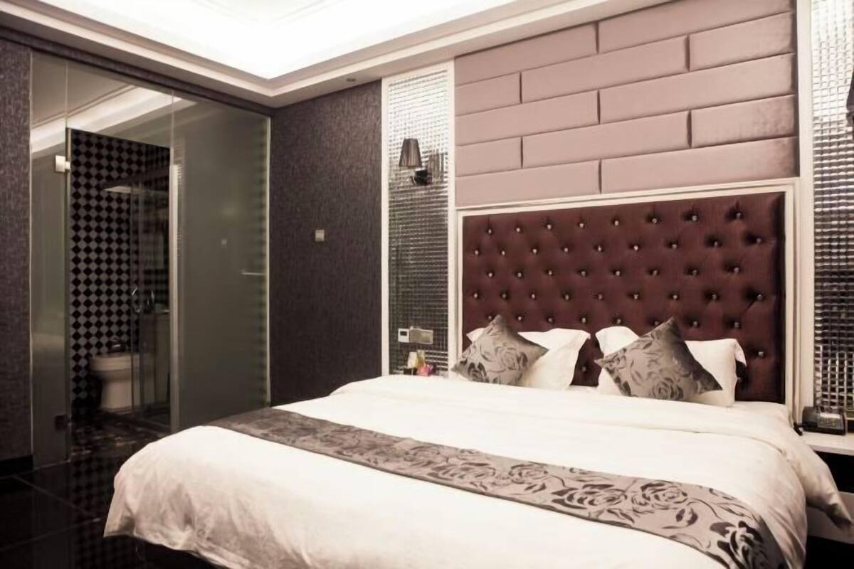 A modern hotel room with a large bed, a glass shower enclosure, and a brick-patterned wall.