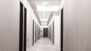 Un pasillo largo y estrecho de hotel con puertas a ambos lados, una lámpara en el techo y un extintor en la pared derecha.