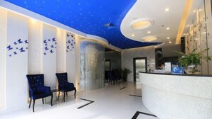 Vestíbulo de hotel con un mostrador de recepción curvo, dos sillas azules, una pared de vidrio y un techo con diseño de estrellas.