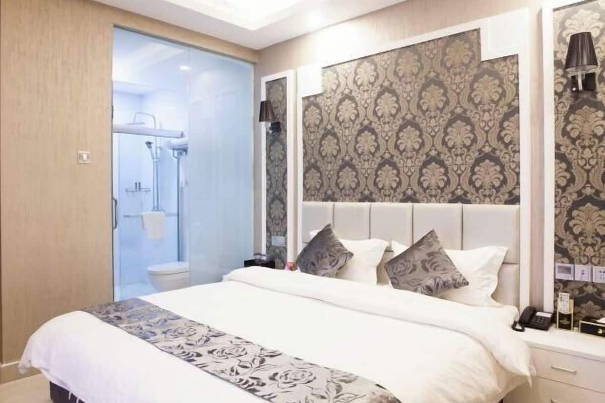 A bedroom with a bed, a nightstand, a mirror, and a bathroom visible through a glass door.
