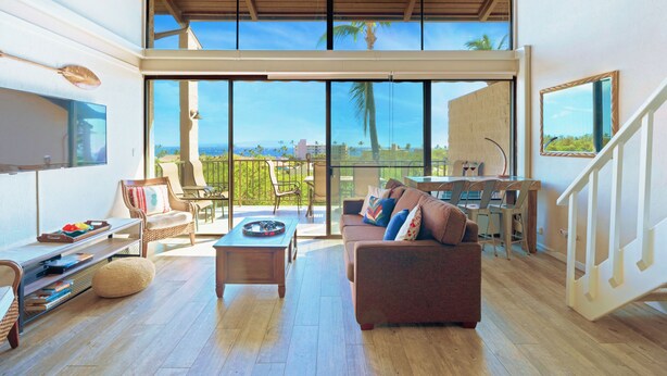 A spacious living area with a large sliding glass door leading to a balcony, a wooden ceiling fan, and a dining area with a table and chairs.