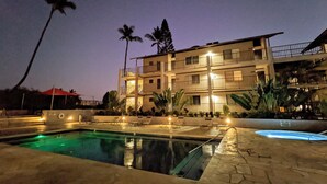 A multi-story hotel with a swimming pool, palm trees, and outdoor seating areas.