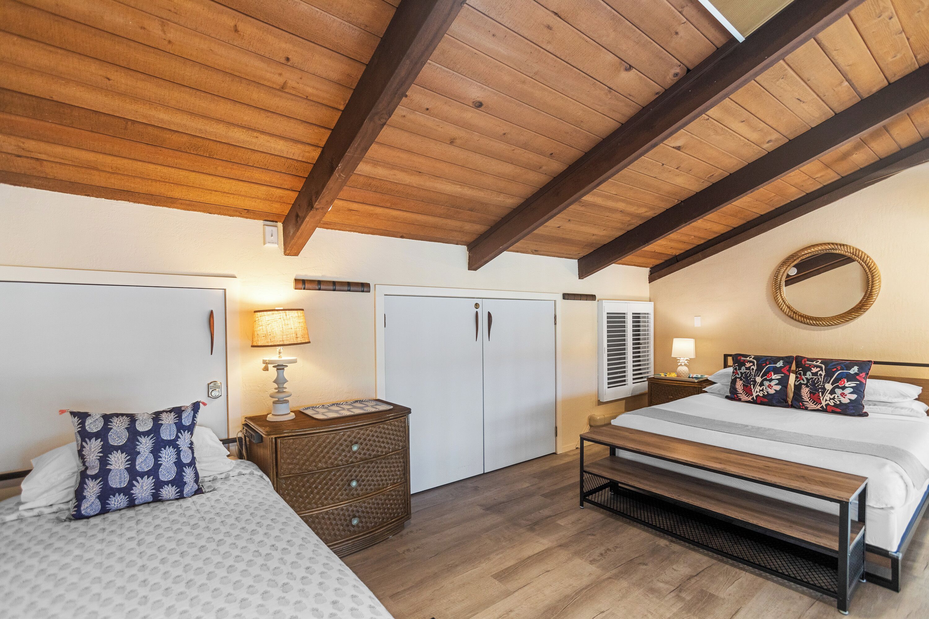 Ein Schlafzimmer mit Holzboden, einem Bett mit weißer, gemusterter Bettdecke, einem Nachttisch mit Lampe und einem Kleiderschrank.
