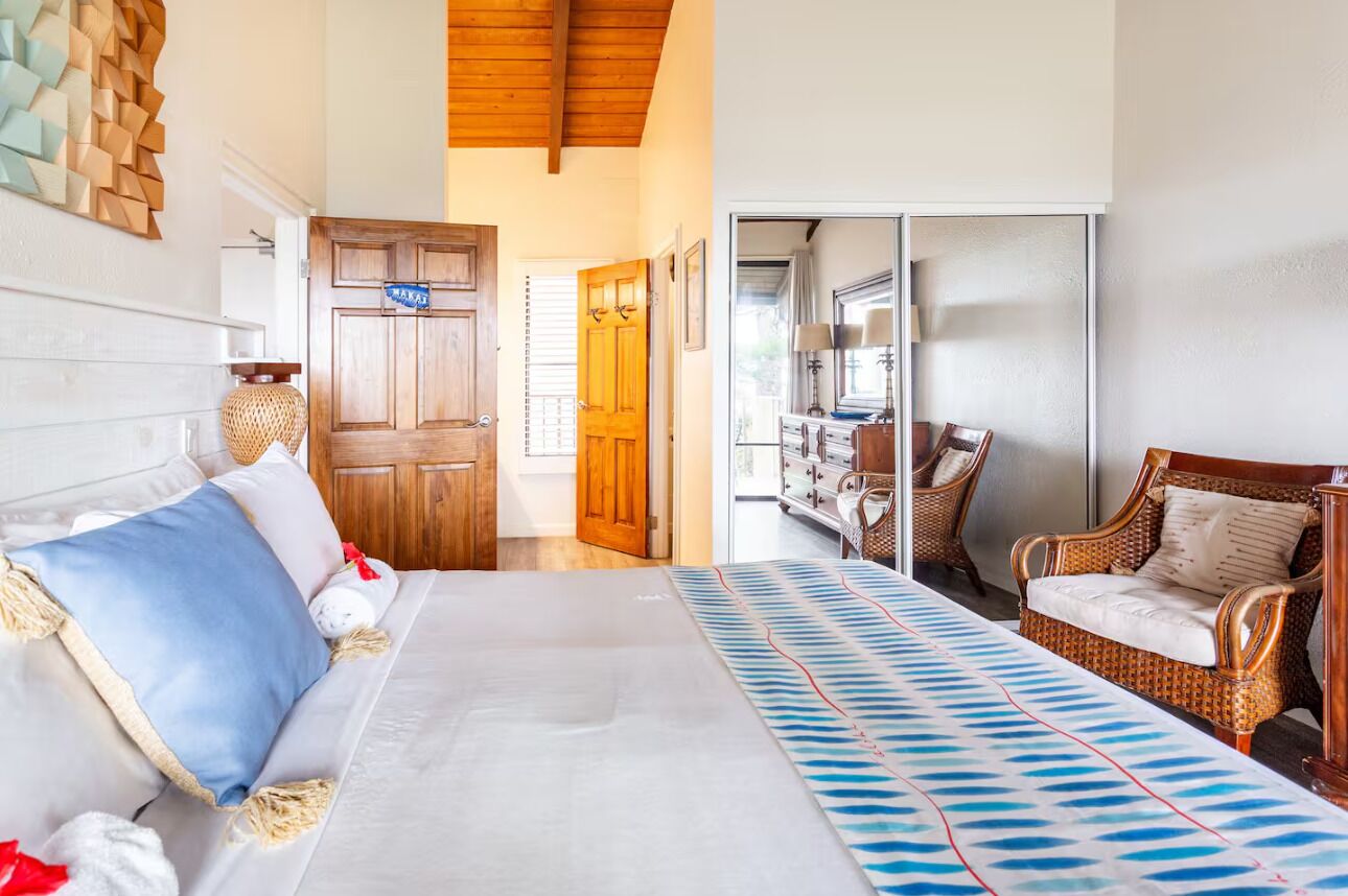 Habitació d'hotel amb un llit, una cadira de vimet, una porta de fusta i vista al bany.
