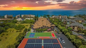 A resort with a tennis court, solar panels, and a view of the ocean at sunset.