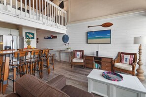 Amplia sala de estar con mesa de comedor, sillas de madera, sofá y televisor montado en la pared.