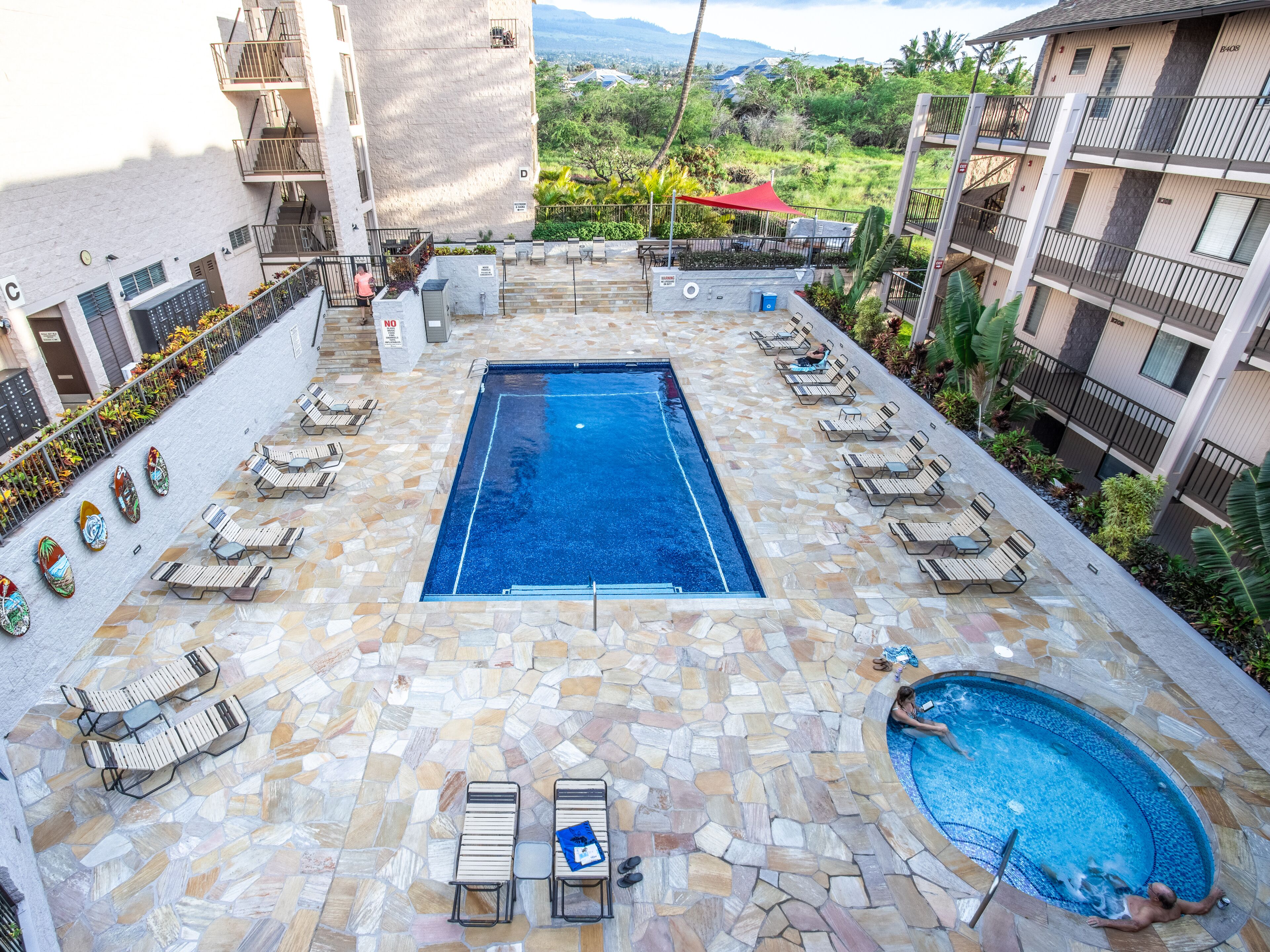 A rooftop pool area with a rectangular pool, lounge chairs, and a smaller circular pool.