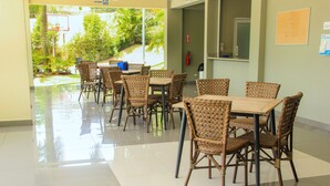 Un área de comedor con sillas y mesas de mimbre, un aro de baloncesto en el exterior y un extintor en la pared.