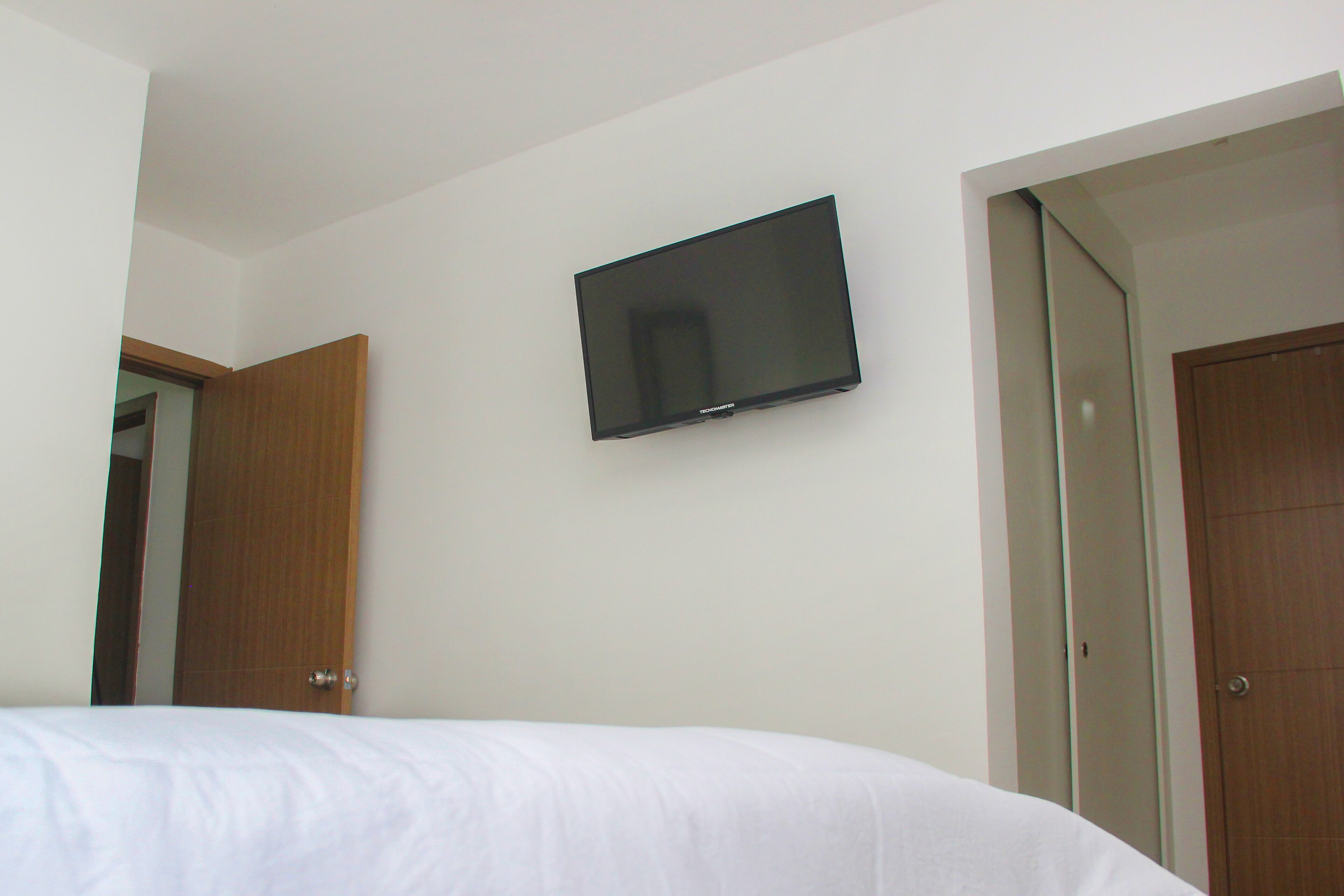 A bedroom with a bed, a television mounted on the wall, and two doors.