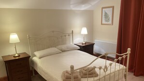 A neatly made bed with a white headboard, a bedside table with a lamp, a nightstand with drawers, and a radiator in the background.