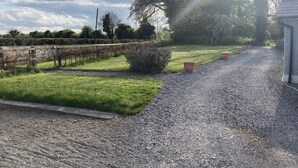 A gravel driveway leading to a building with a stone wall and a grassy area with a hedge and potted plants.