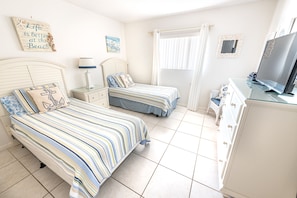 A bedroom with two beds, a TV, a dresser, and a window with curtains.