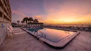 A swimming pool with lounge chairs and a view of palm trees at sunset. - Oceanfront 2BR 2BA Condo 5th Floor Balcony Ocean Views, 504 (Indian Harbour Beach)